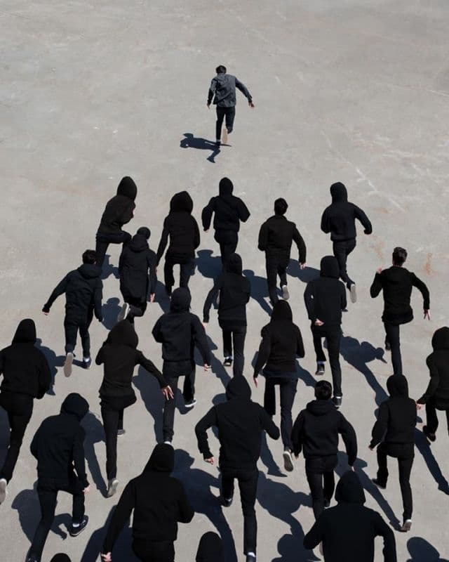 Grupo de pessoas vestidas de preto correndo sobre uma superfície de concreto, visto de cima.