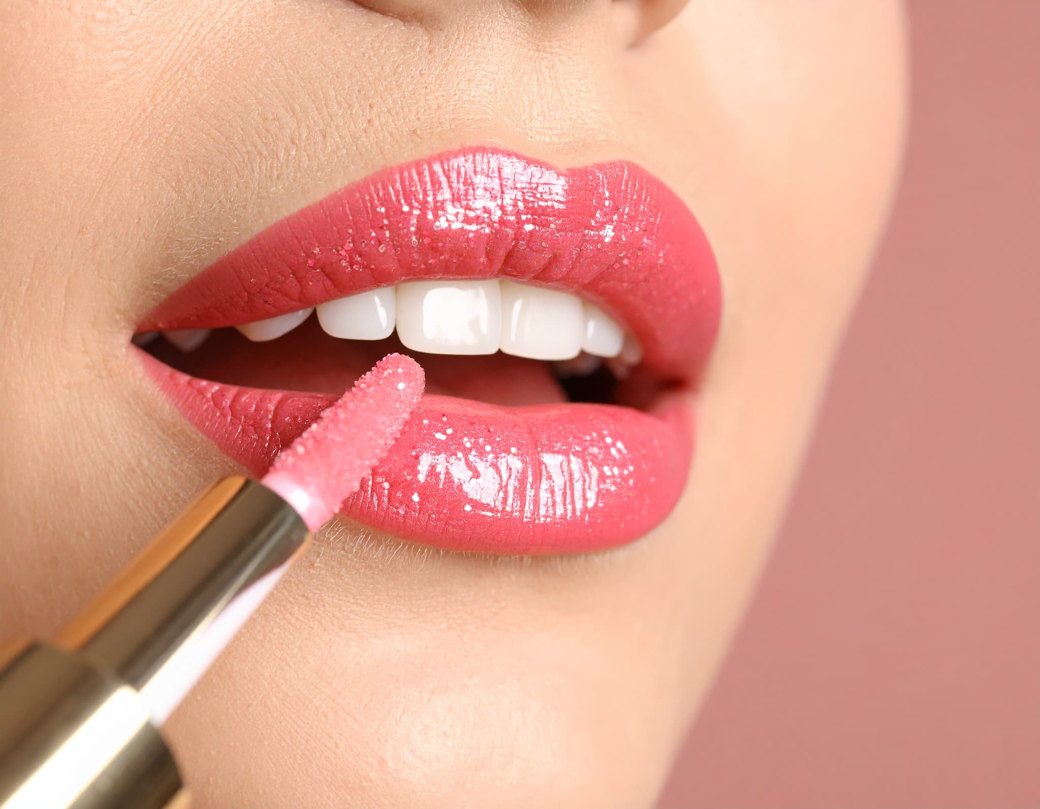 Detalhe da aplicação de gloss rosa nos lábios.