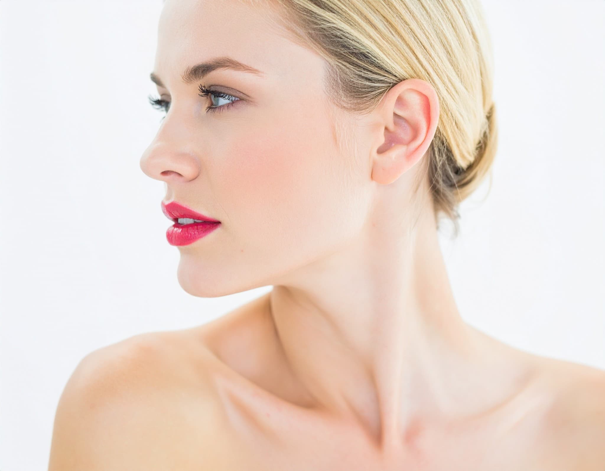Retrato de perfil de mulher com cabelo preso e batom rosa sobre fundo branco.