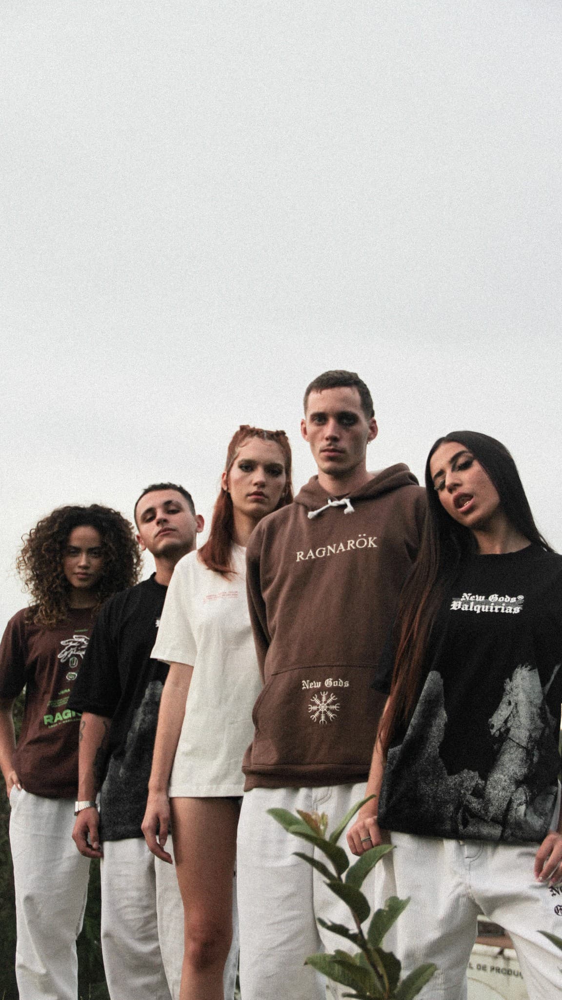 Cinco modelos com peças NEW GODS, fotografados de baixo contra o céu nublado.
