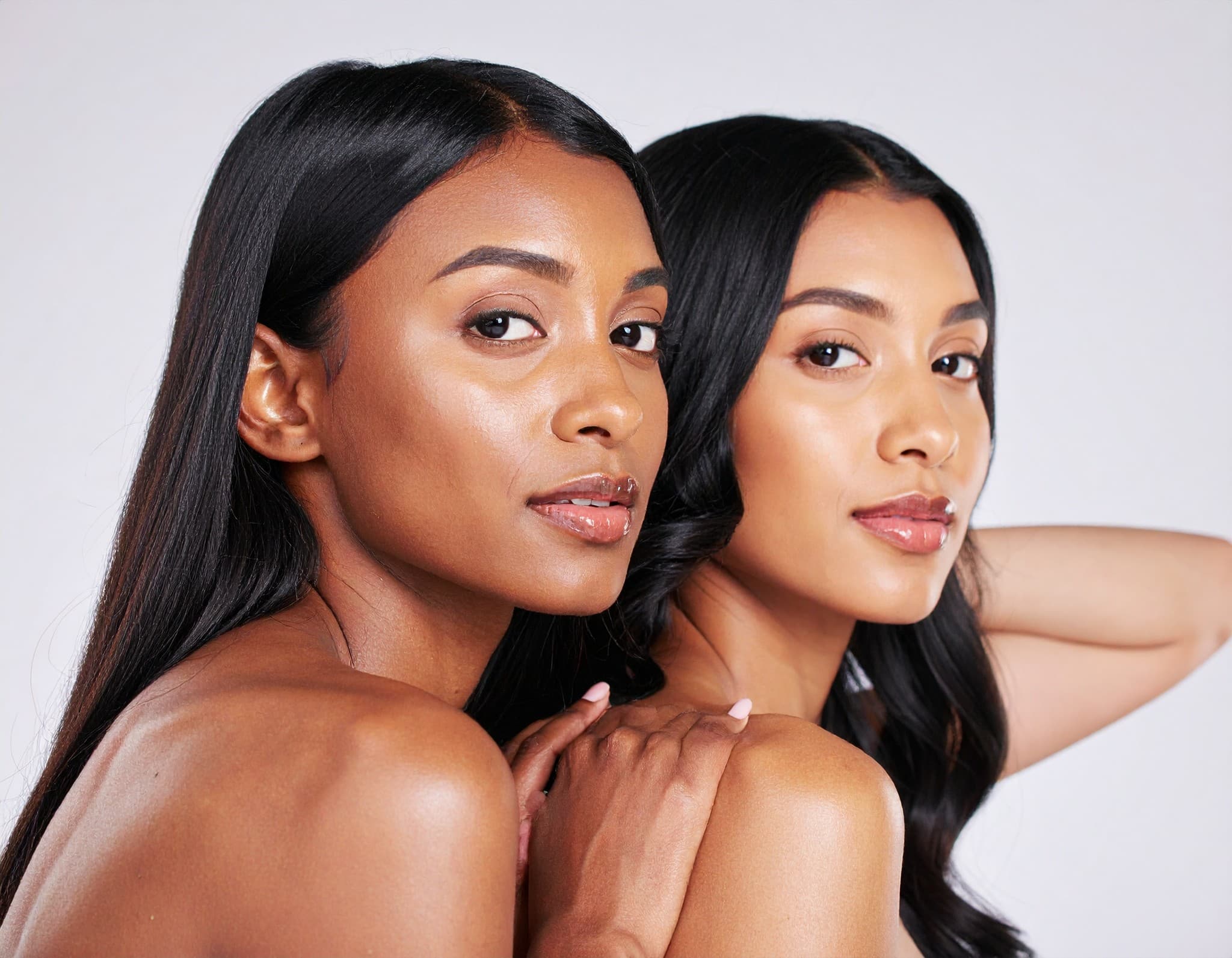 Duas mulheres com maquiagem em tons naturais, fotografadas juntas sobre fundo claro.