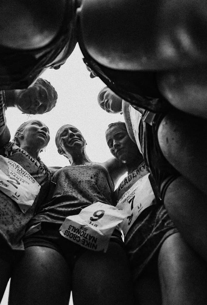 Grupo de corredoras reunidas em círculo, visto de baixo em fotografia em preto e branco.